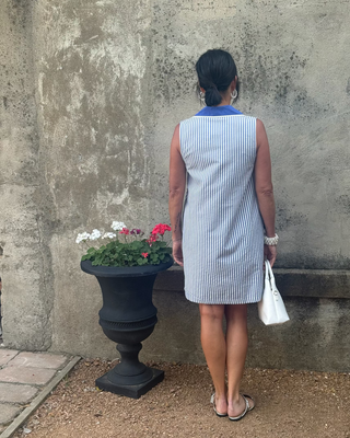 Woman in a bue & white striped dress against a wall next to flowers