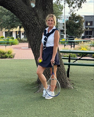 Woman holding a tennis racket and ball on a tennis court with a tree in the background