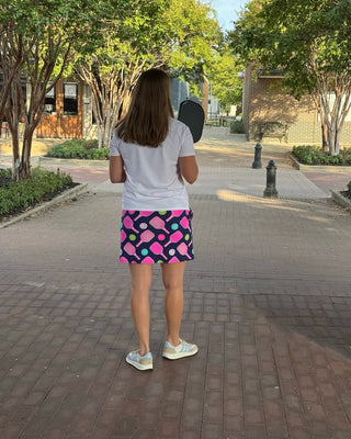 Person standing on a sidewalk wearing a colorful skirt and white sneakers.