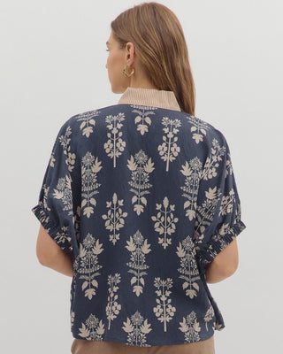 Woman wearing a navy floral patterned blouse with beige pants on a white background