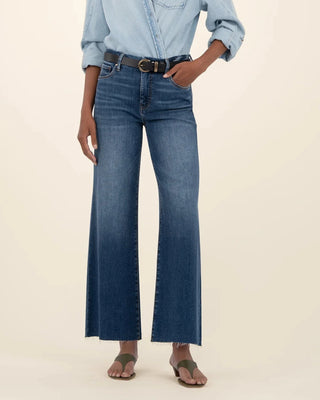 Person wearing a light blue denim shirt and dark blue jeans on a beige background