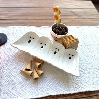Halloween-themed snack setup with ghost-shaped plates, cookies, and a small bowl on a wooden table.