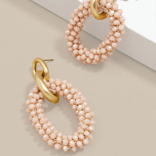 Pair of pink beaded hoop earrings with gold links on a light beige background